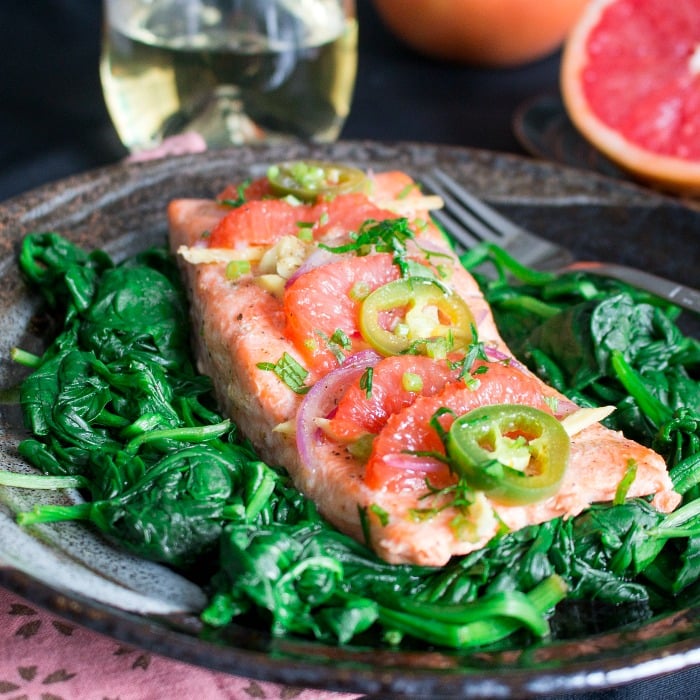 Spicy Citrus Baked Salmon Packets laid open on a bed of cooked spinach.