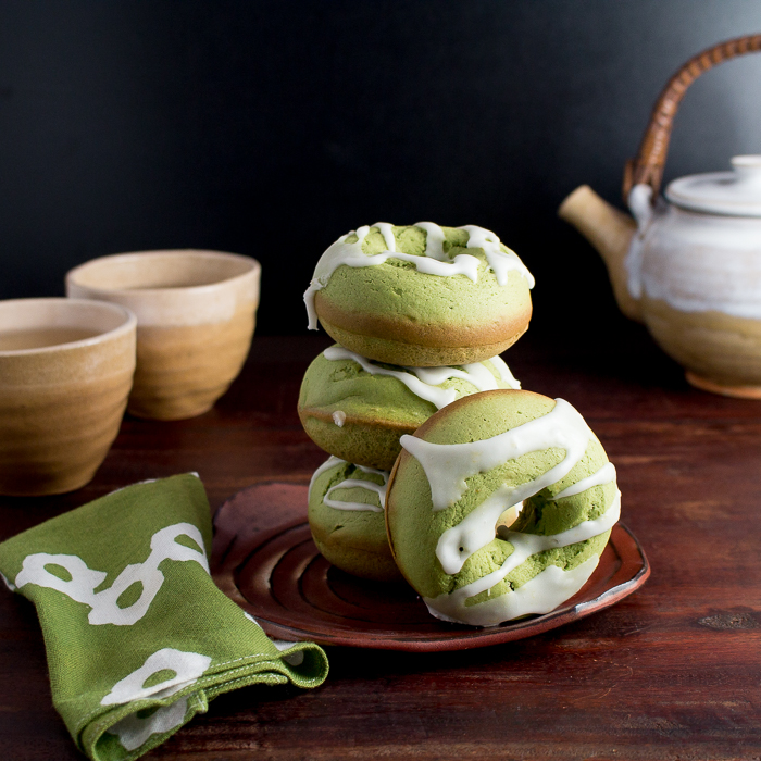 Baked Matcha Lemon Glazed Donuts stacked on a hand made pottery plate with tea pot and cups.