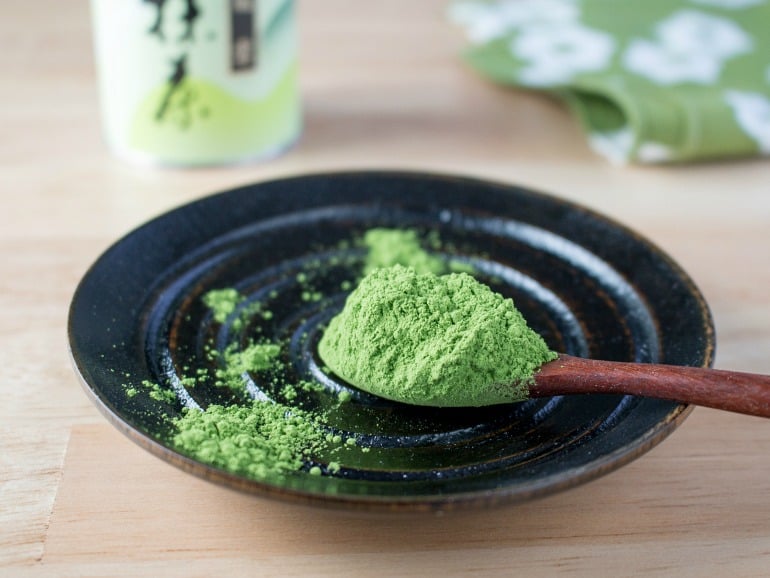 Ceremonial grade matcha on a wooden spoon over a black plate.