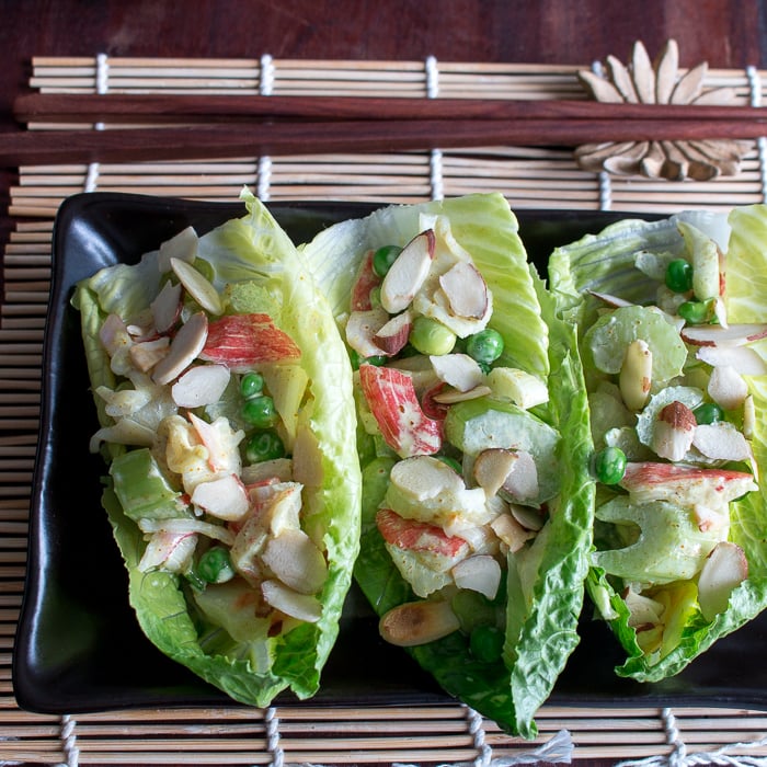 3 lettuce cups filled with crab salad on a black plate with chopsticks on a Japanese mat. 