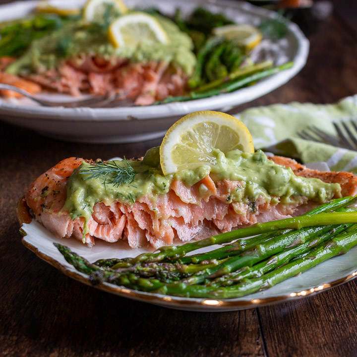 Slice of salmon with the crema on top on a white plate. 