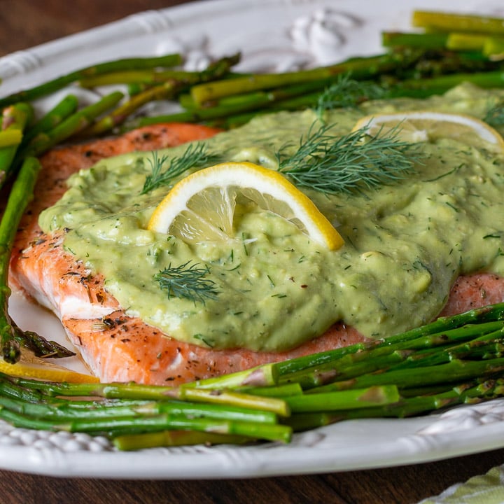 Baked salmon with avocado sauce on top with asparagus on a white serving platter.