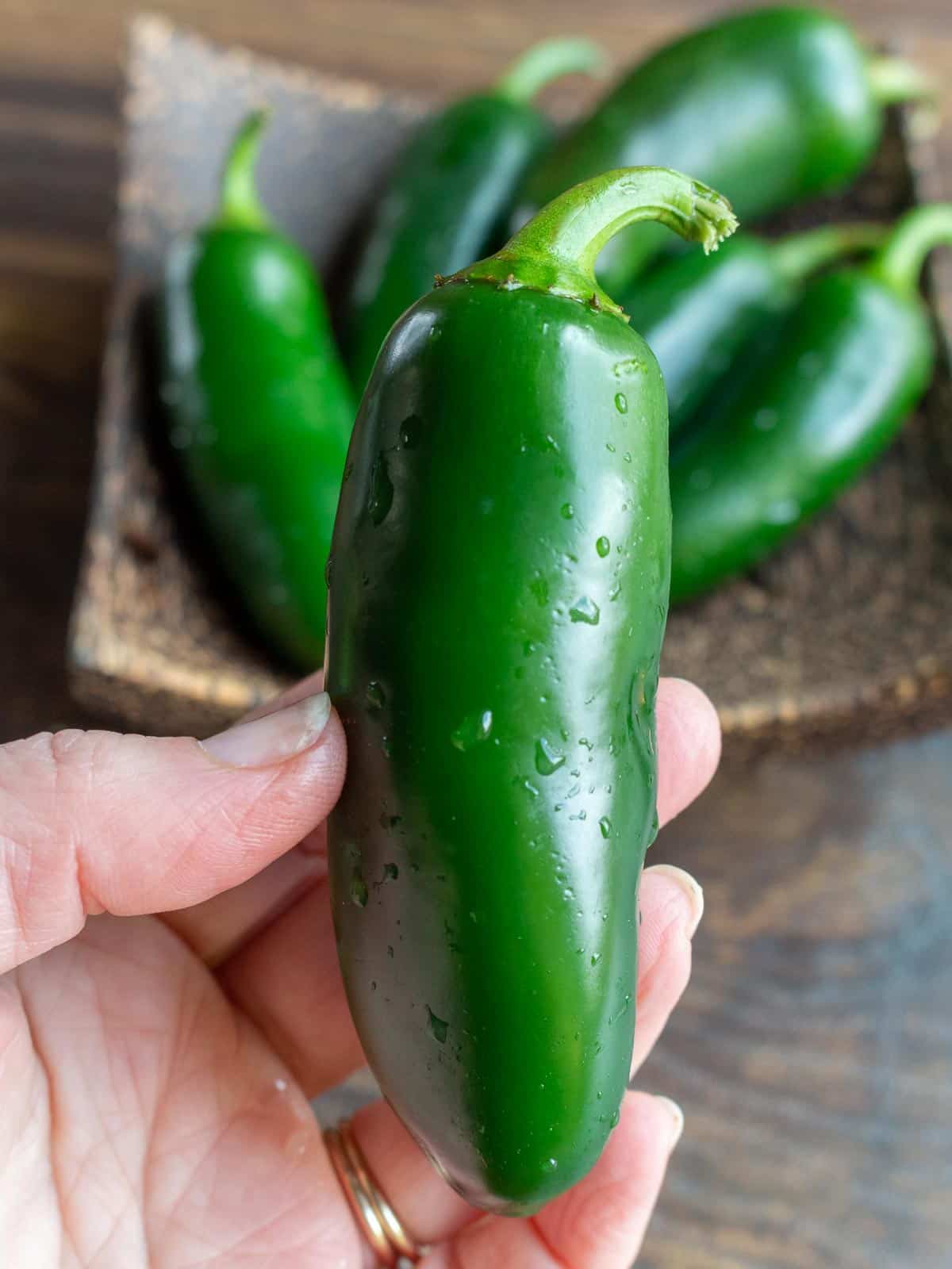 Holding a ripe jalapeno over a wooden bowl of them.