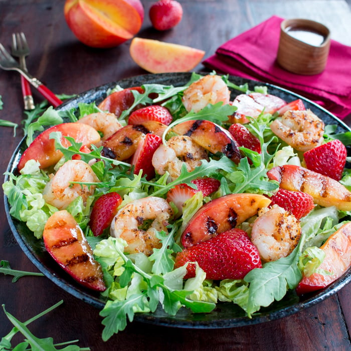 Delicious plate of salad with grilled shrimp, necatrines with dressing on the side.