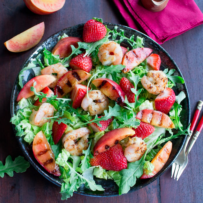 Summer salad in a black bowl with nectarines on the side.