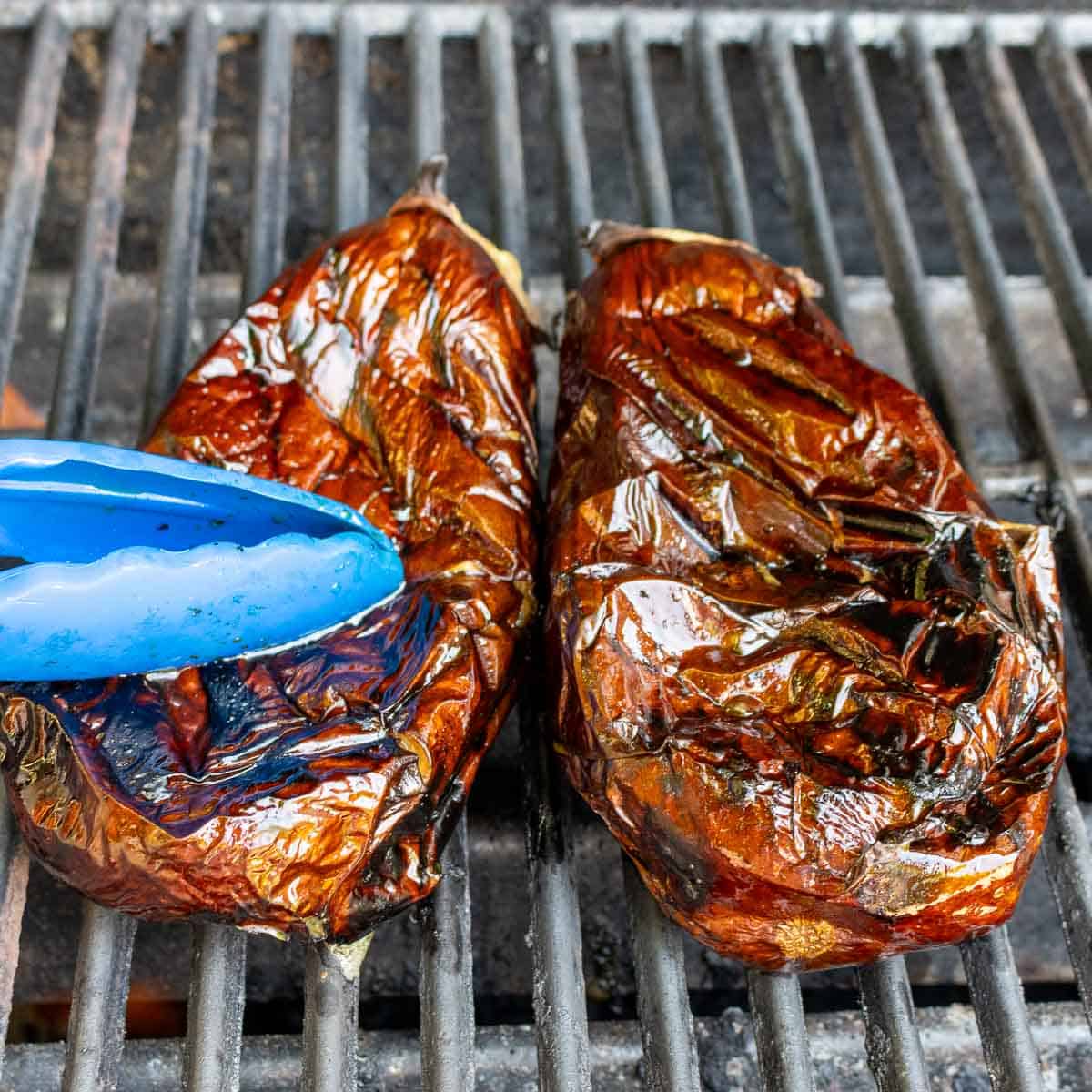 Grilled eggplants are charred and are flat and pressed down with tongs - cooked!