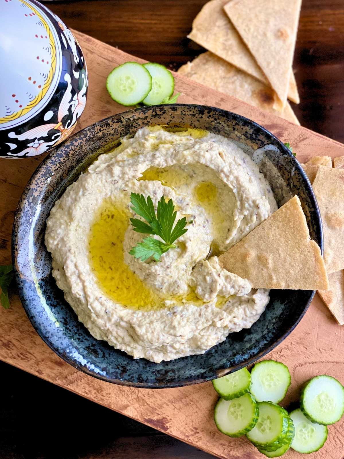 Creamy baba ganoush served with warm flatbreads and sliced cucumbers on a wooden board.