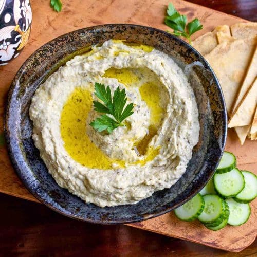 Traditional Lebanese baba ganoush topped with a drizzle of olive oil in a dark black and brown shallow bowl.