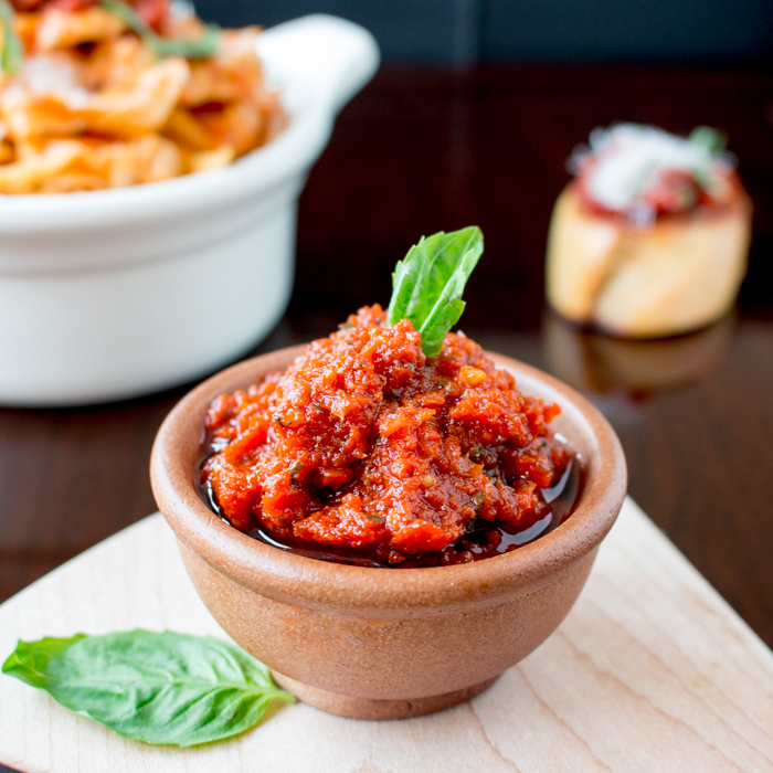 3-Minute Vegan Sun-Dried Tomato Pesto in a wooden bowl with a bowl of pesto pasta in the background.