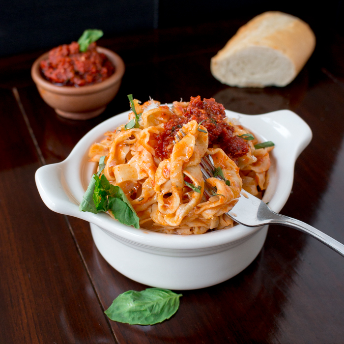 A delicious bowl of pasta with pesto and extra pesto in the background. 