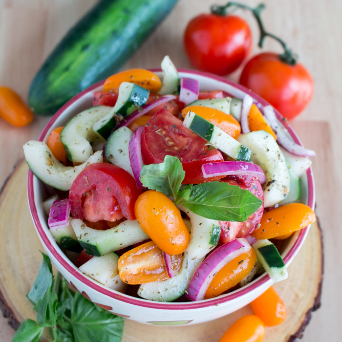 Heirloom Tomato Cucumber Salad in a white and maroon bowl garnished with fresh basil. 