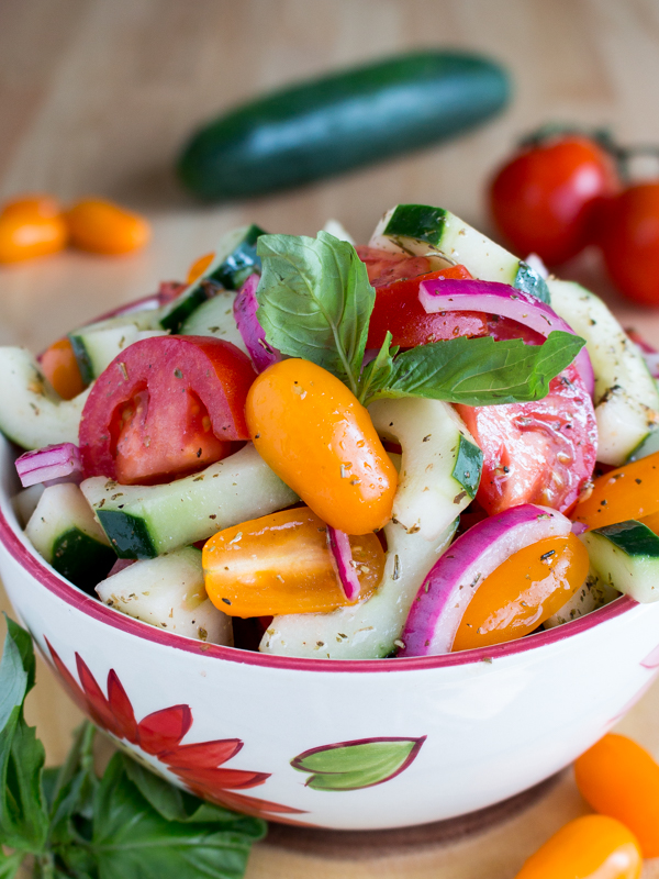 Close up shot of salad garnished with fresh basil with fresh garden veggies in the background.