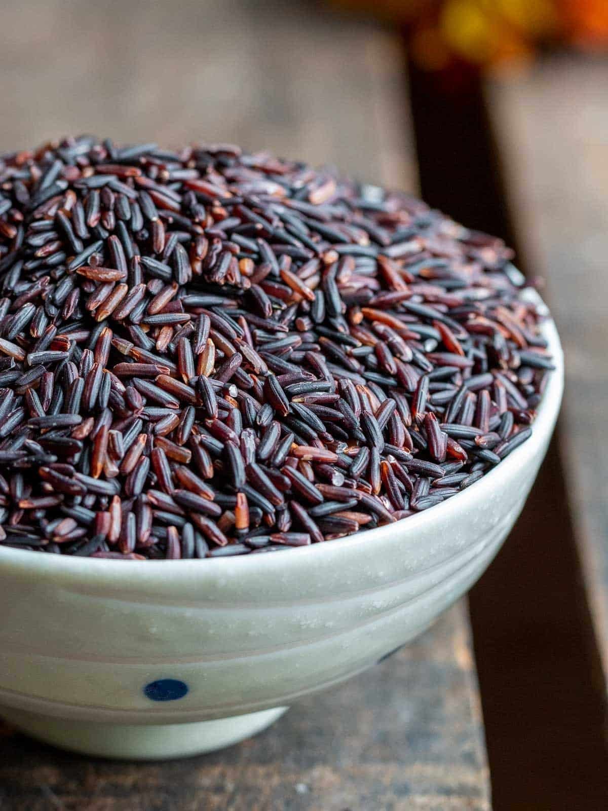 Dry Thai Jasmine Black rice in a white bowl on a wooden board.