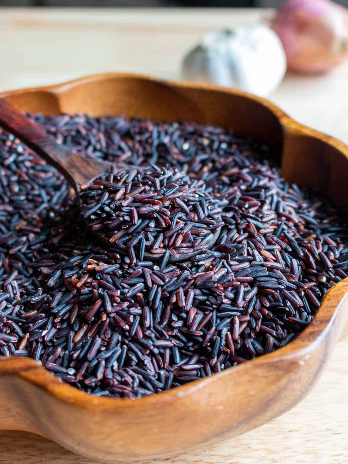 Dry forbidden black rice scooped in spoon in a wooden bowl. 
