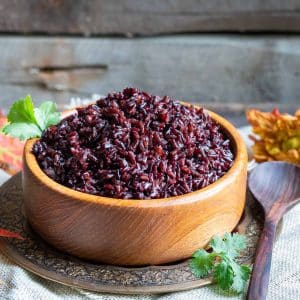 Cooked Instant Pot black rice pilaf in a wooden bowl with a wooden spoon.