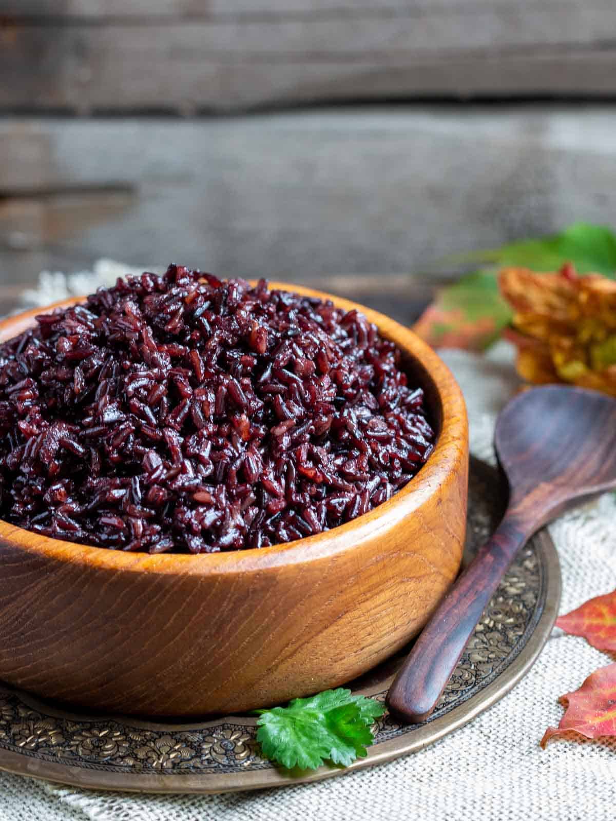 Cooked Instant Pot black rice pilaf in a wooden bowl with fall leaves around bowl.