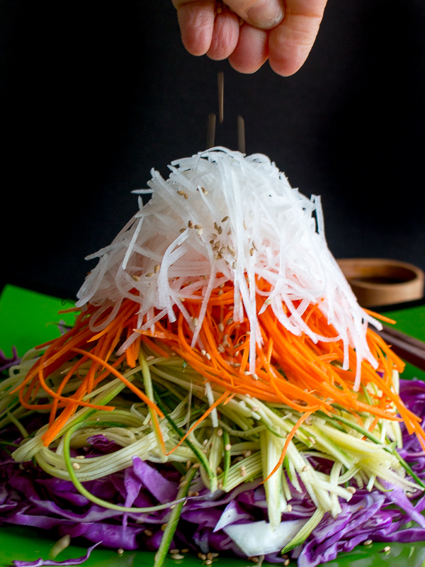 Sprinkling of sesame seeds going on top of the mountain high layered Asian salad