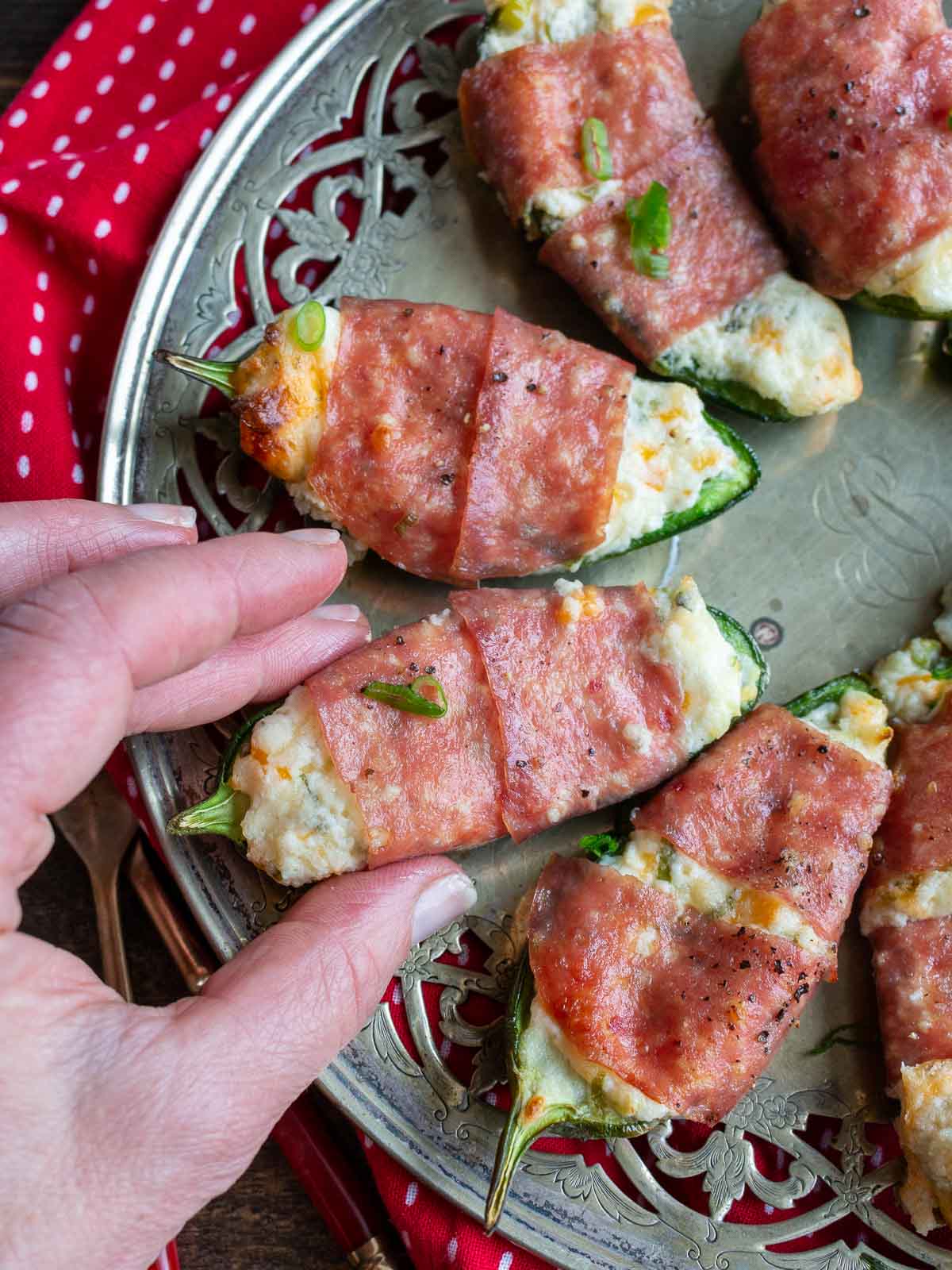 Air fried jalapeno poppers on a silver platter with a hand grabbing one off the plate. 