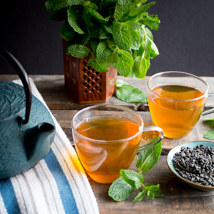 2 cups filled with Moroccan mint tea and teapot and mint and looseleaf tea