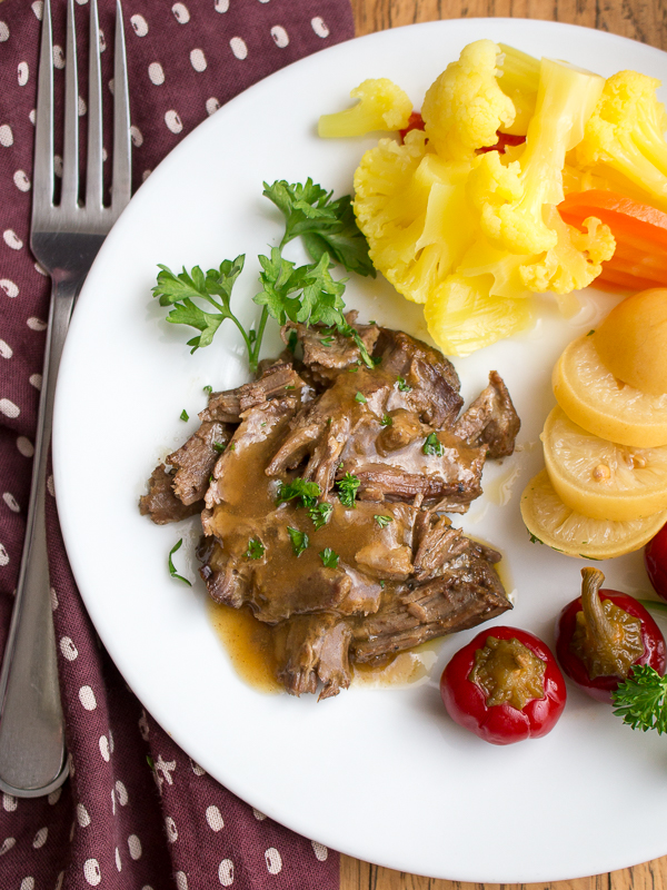 Top down photo of pulled apart tender lamb with gravy and assorted pickles