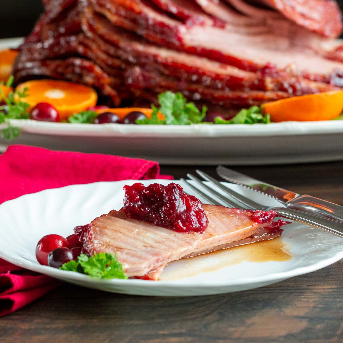 Slices of air fryer baked ham on a white plate with a dollop of cranberry sauce on top.