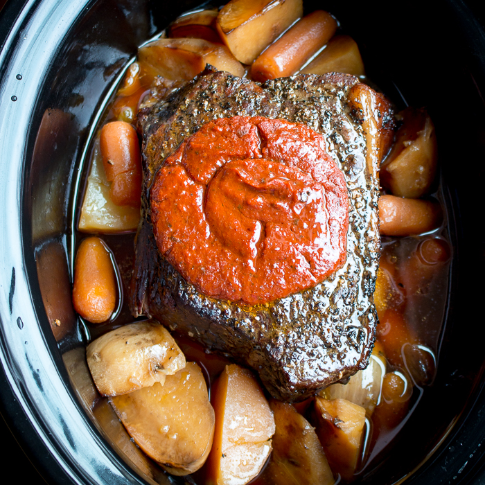 The whole cooked beef roast in the slow cooker with tomato sauce on top.