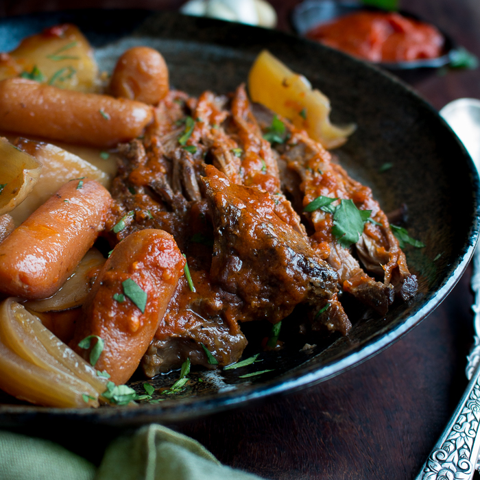 Saucy Italian Slow Cooker Pot Roast with onions and carrots on a black plate.