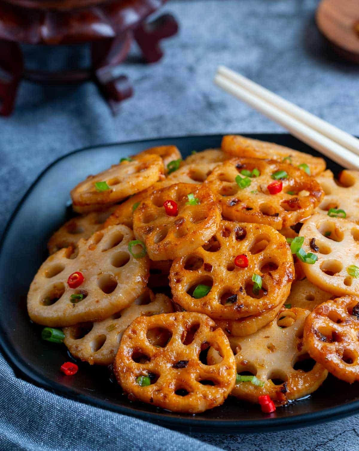 Prepared lotus root stir fry on a black plate garnished with chili and green onions.