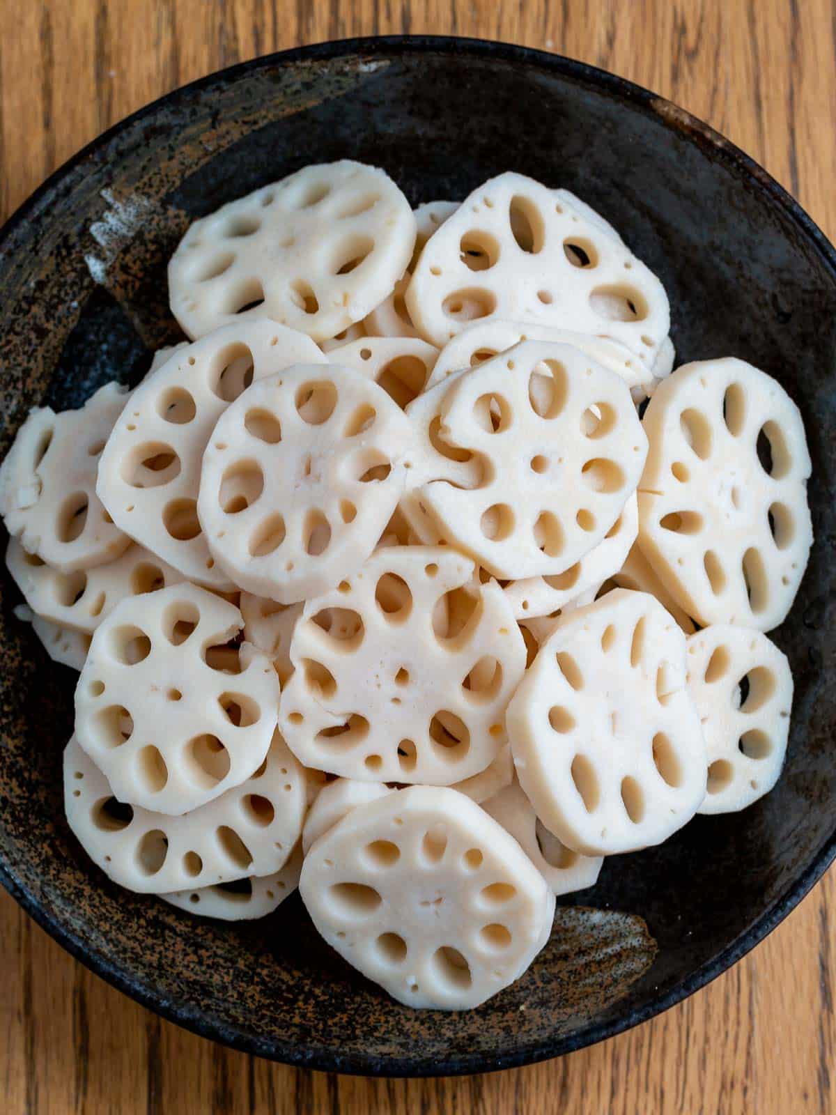 Raw lotus root with 9 holes peeled and sliced on black plate.