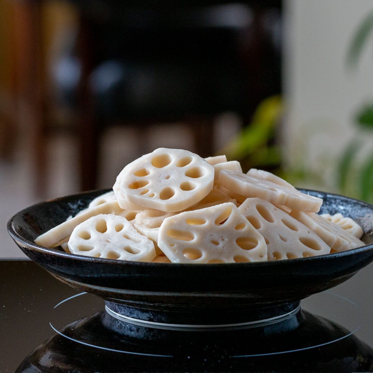 Raw Lotus roots sliced and in a black bowl.
