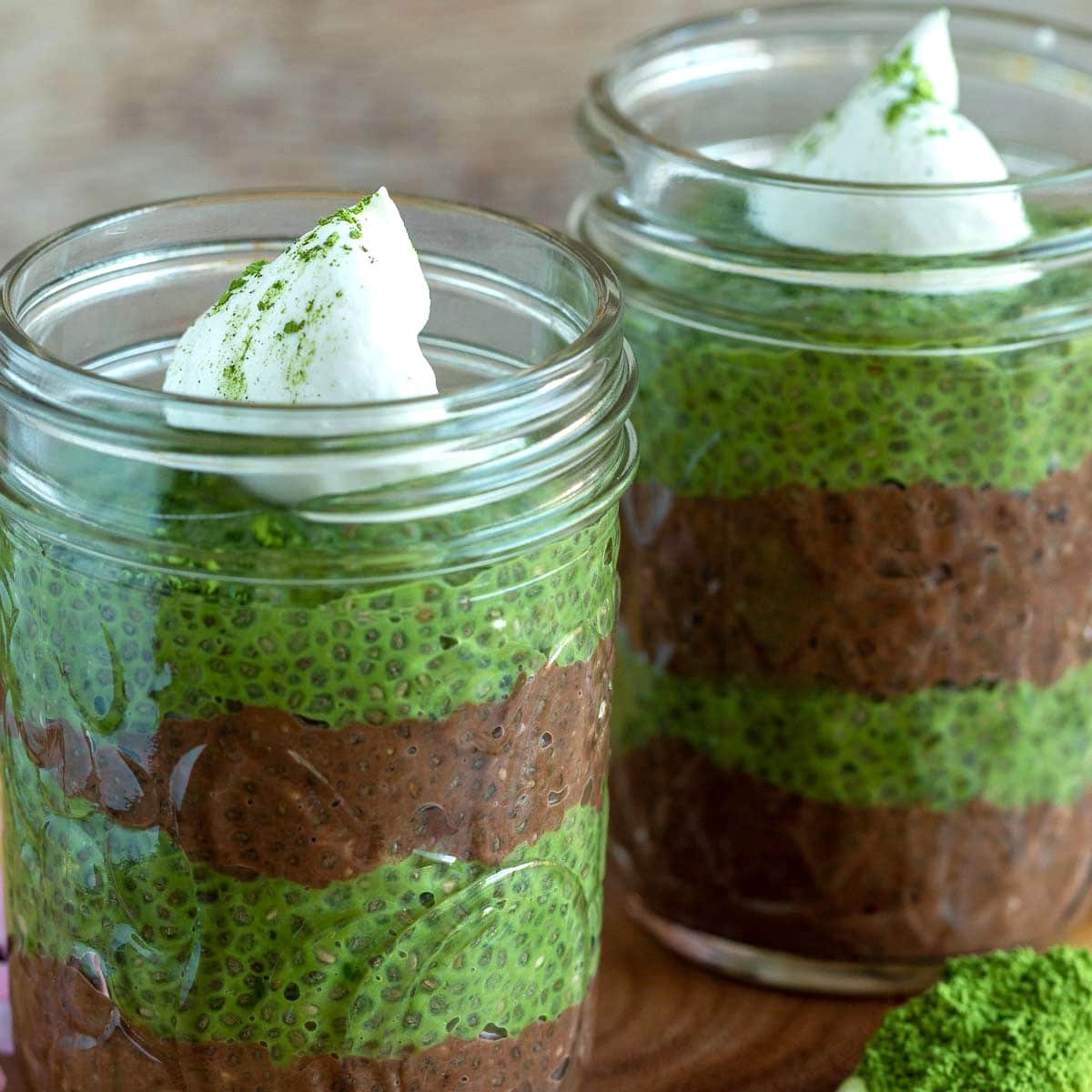 Chocolate and matcha chia seed puddings in mason jars with a scoop of matcha green tea powder.