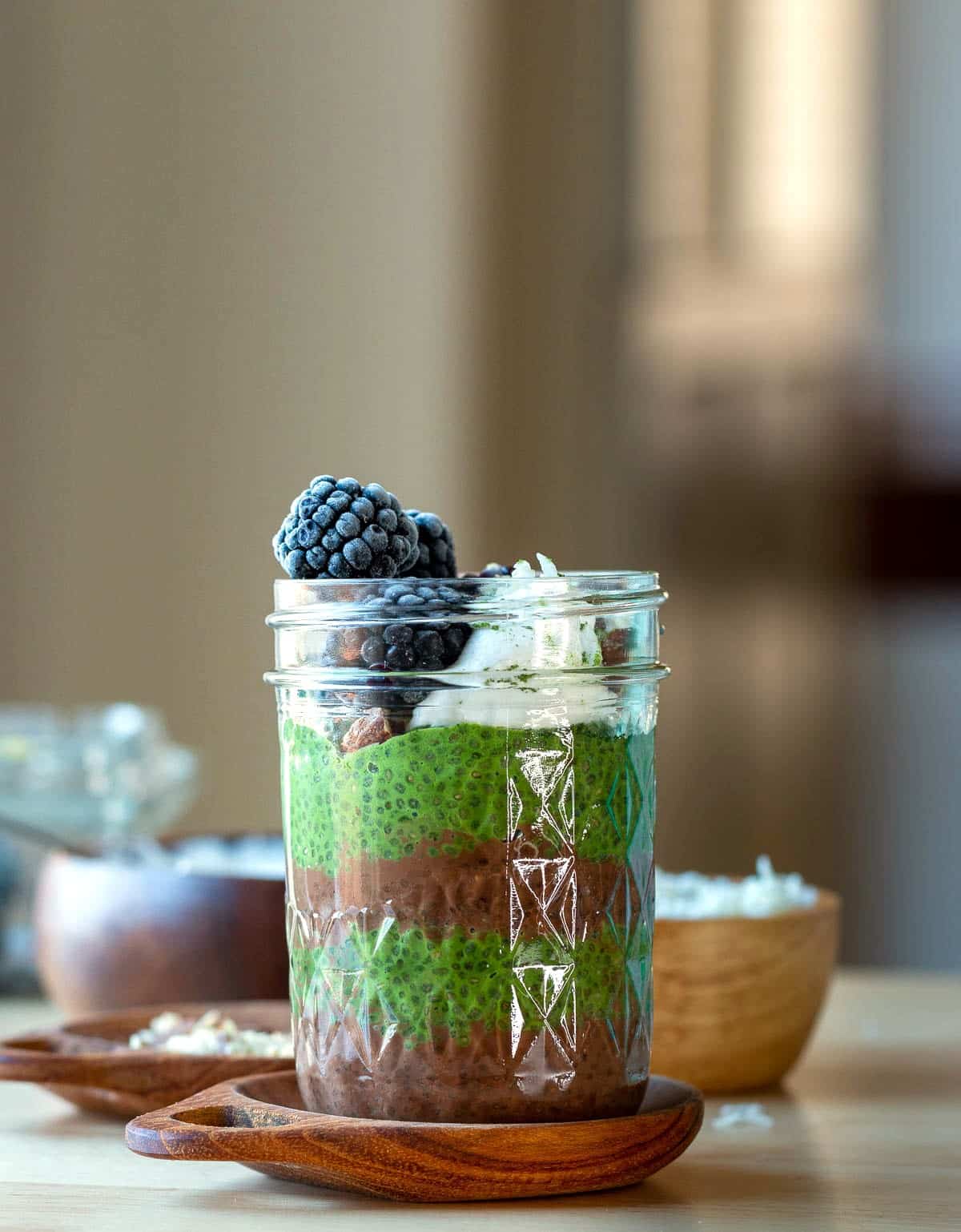 Garnished with coconut cream and berries, cocoa and green tea chia seed parfait on a wooden plate.