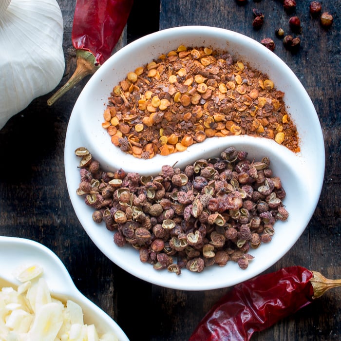 Close up of red pepper flakes and Sichuan peppercorns in a yin and yang white dish.