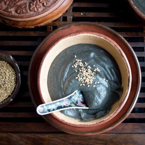 Creamy black sesame dessert soup with a spoon in a handmade brown pottery bowl.