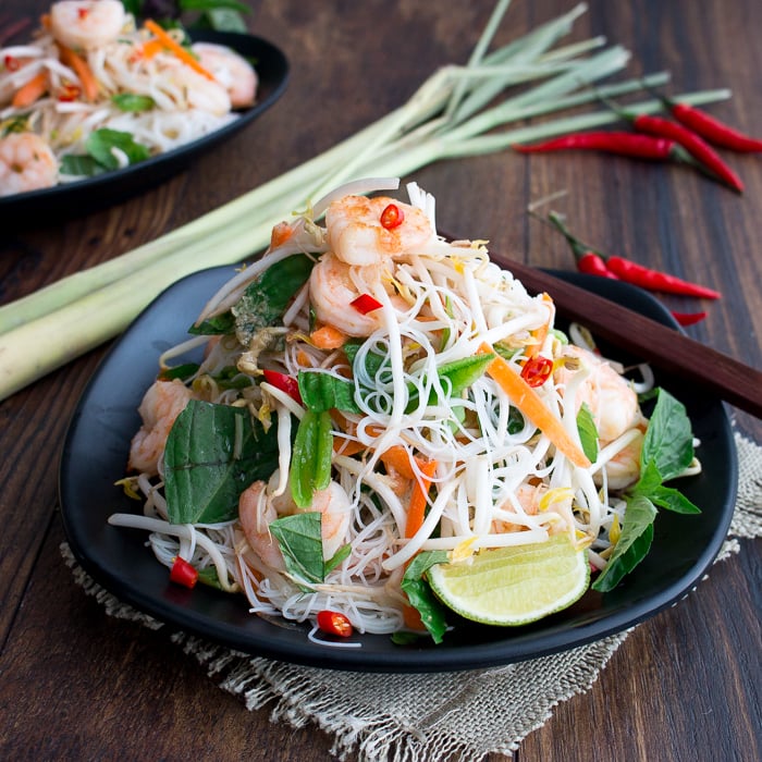 Vietnamese Shrimp Vermicelli Salad stacked high on a black plate with lemon grass and chili peppers scattered around the plate. 