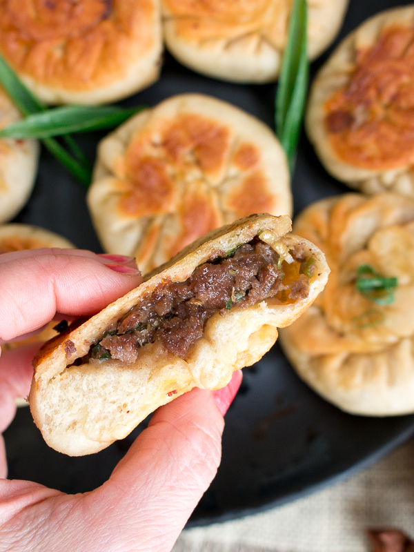 Holding a Pan Fried Beef Bao in hand and cut in half showing the juicy beef inside. 