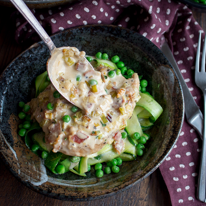 Creamy bacon sauce getting drizzled over a chicken breast.