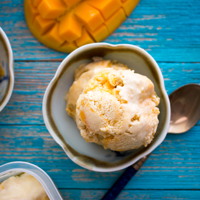 Top down photo showing the mango icecream just starting to melt a little with a spoon and a cut mango in the background.