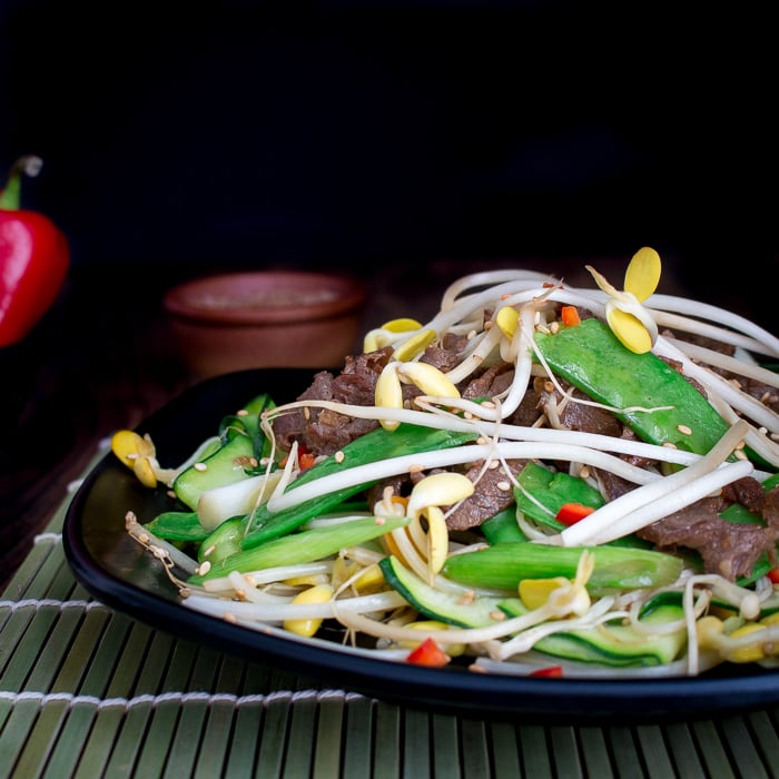 Beef and vegetable stir fried on a black serving plate with a green placemat underneath.