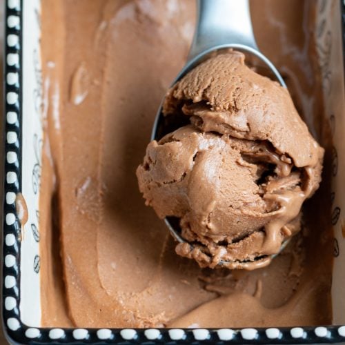 Scoop of Mocha Banana Ice Cream in a ice cream scooper in a black and white ceramic bowl.