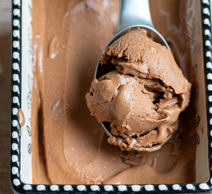 Scoop of Mocha Banana Ice Cream in a ice cream scooper in a black and white ceramic bowl.