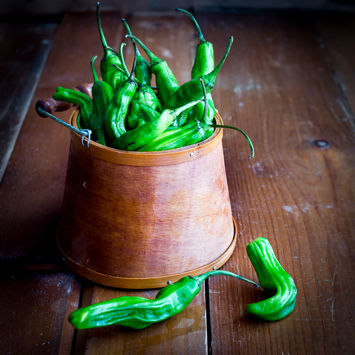 Basket of raw shishito peppers in a wooden bucket.