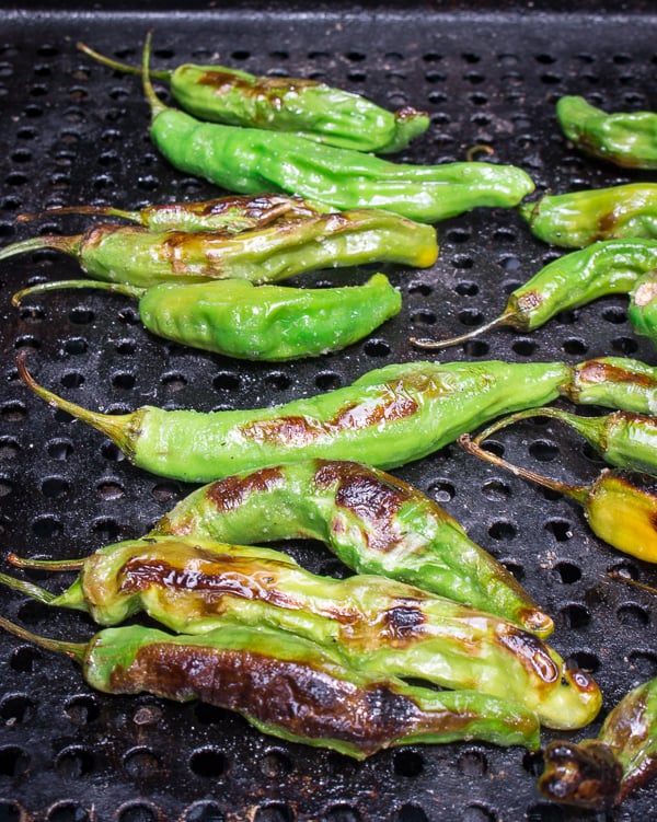 Shishito peppers grilling on a grill plate on the BBQ.