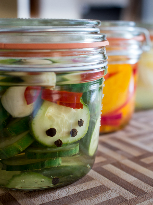 3 different type of refrigerator pickles in glass containers on a cutting board. 