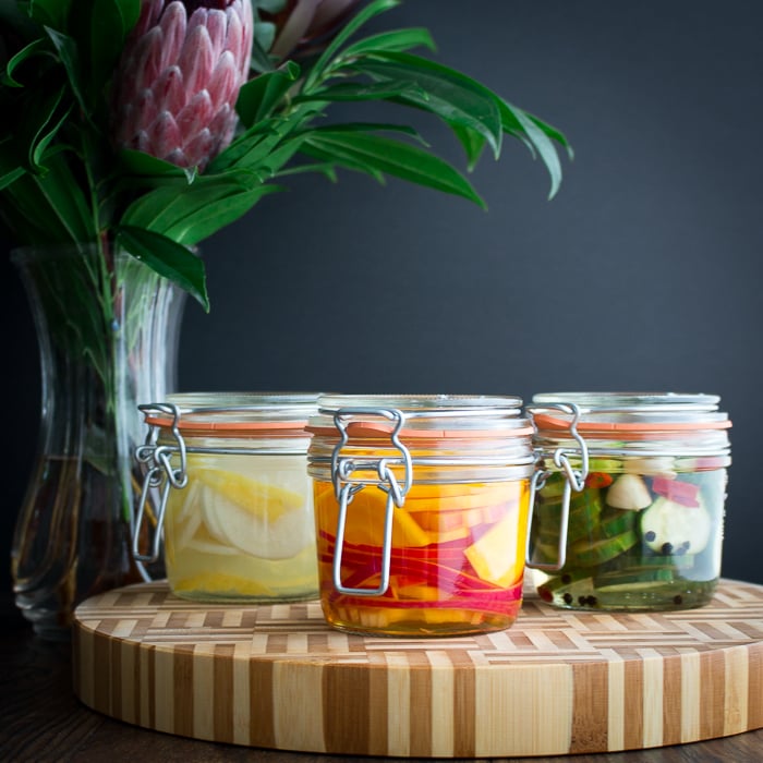 3 different kinds of refrigerator pickles on a wooden cutting board in glass canning jars. 