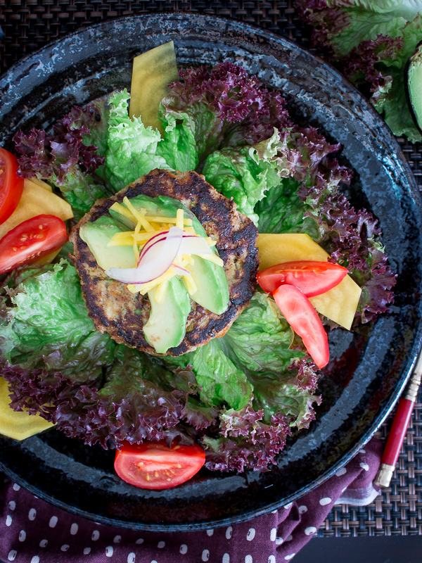 Burgers with avocado and tomato toppings on a black plate.