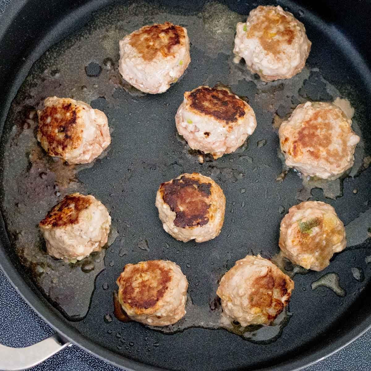 Thai turkey tofu meatballs getting seared in a pan on the stovetop. 