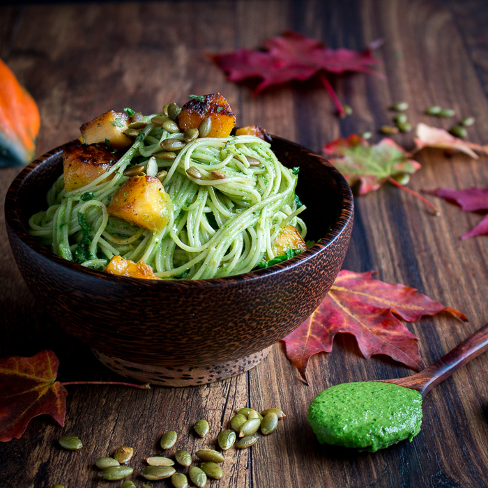 a bowl of one pot creamy kale pasta in a brown bowl with leaves and a pumpkin on the table.