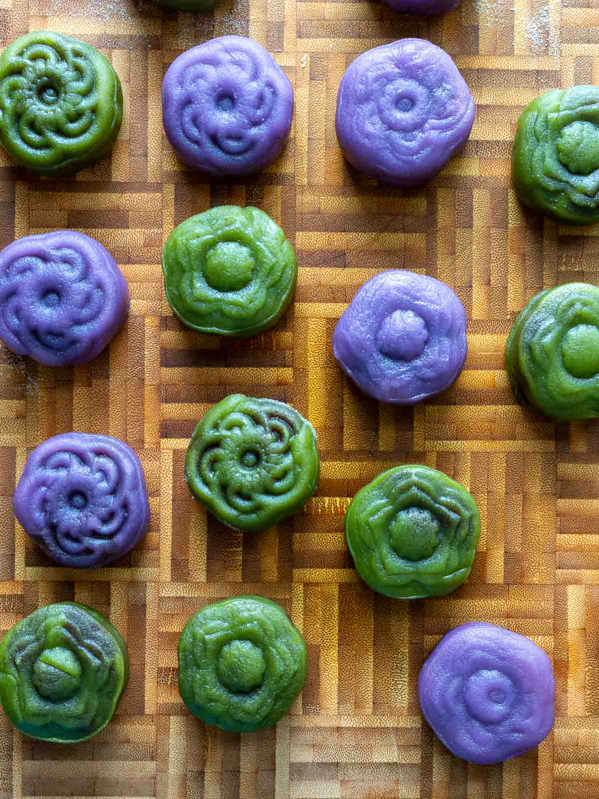 Green matcha and purple Ube crystal ice skinned mooncakes on a wooden cutting board.