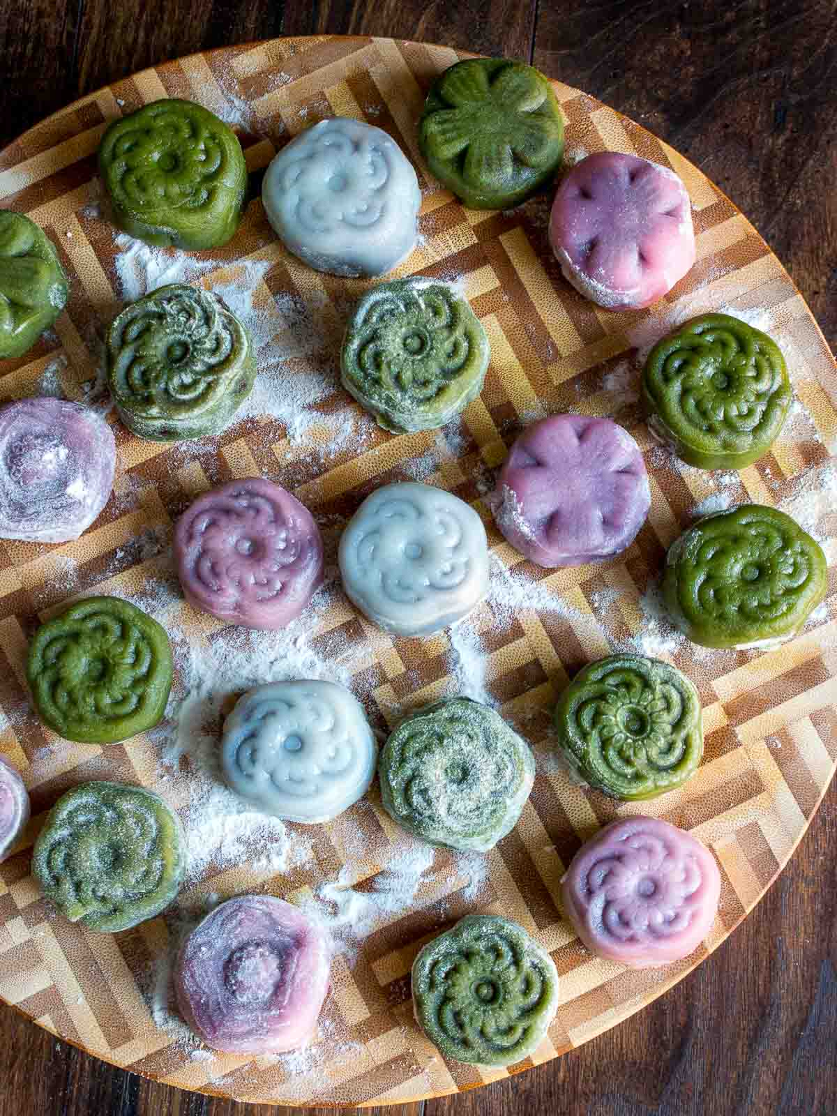 Displaying many prepared green, white and pink snow skin mooncakes laying on a wooden board. 